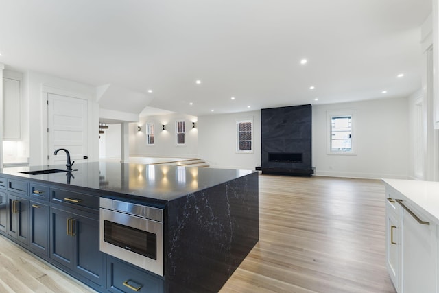 kitchen featuring sink, white cabinetry, a center island with sink, stainless steel microwave, and a premium fireplace