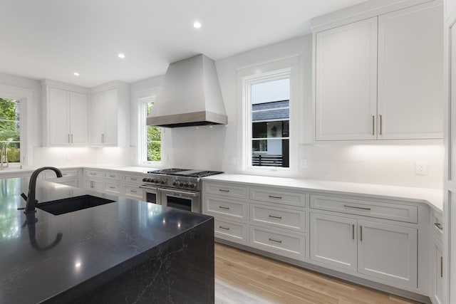 kitchen featuring premium range hood, sink, light wood-type flooring, a healthy amount of sunlight, and range with two ovens