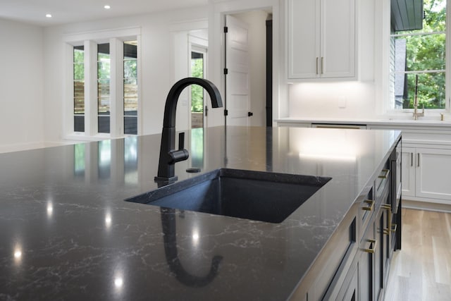 details featuring white cabinetry, sink, light hardwood / wood-style flooring, and dark stone countertops