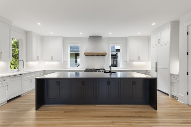 kitchen with custom exhaust hood, white cabinetry, a kitchen island with sink, and light wood-type flooring