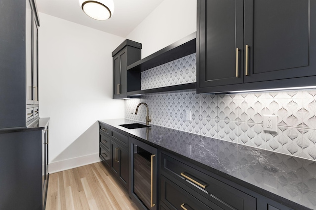 kitchen with wine cooler, sink, dark stone countertops, light hardwood / wood-style floors, and backsplash