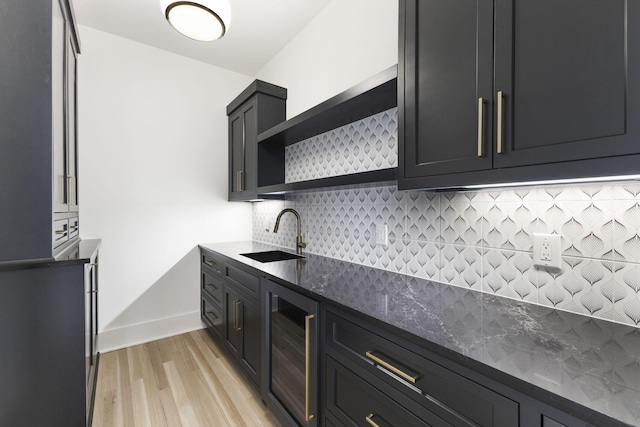 kitchen with sink, backsplash, beverage cooler, dark stone counters, and light wood-type flooring