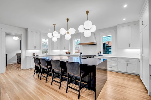 kitchen featuring premium range hood, a breakfast bar, decorative light fixtures, white cabinetry, and an island with sink