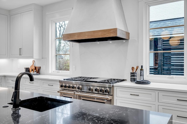 kitchen featuring premium range hood, sink, stone countertops, range with two ovens, and white cabinets