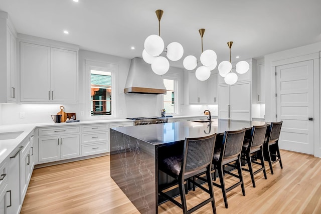 kitchen with decorative light fixtures, an island with sink, white cabinetry, a breakfast bar area, and custom exhaust hood