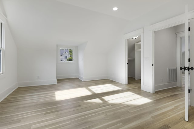 unfurnished bedroom featuring light hardwood / wood-style flooring, a walk in closet, and vaulted ceiling