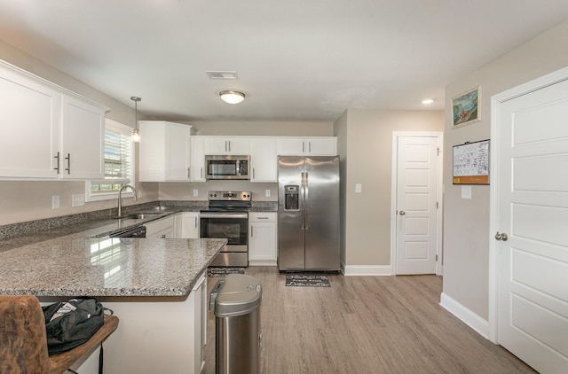 kitchen featuring pendant lighting, kitchen peninsula, sink, white cabinetry, and appliances with stainless steel finishes