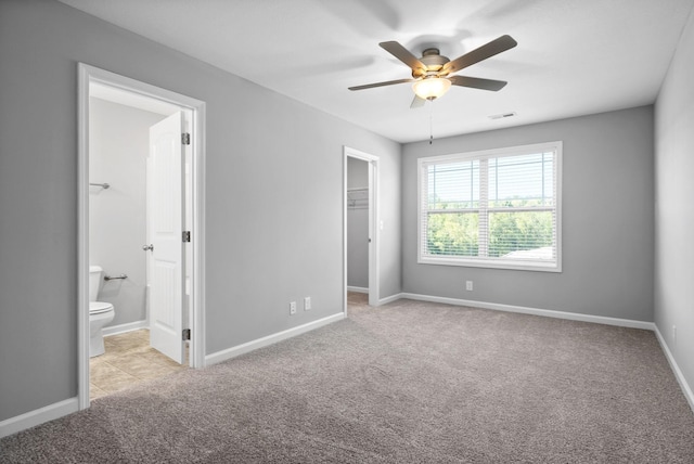 unfurnished bedroom with light carpet, ensuite bath, ceiling fan, a spacious closet, and a closet