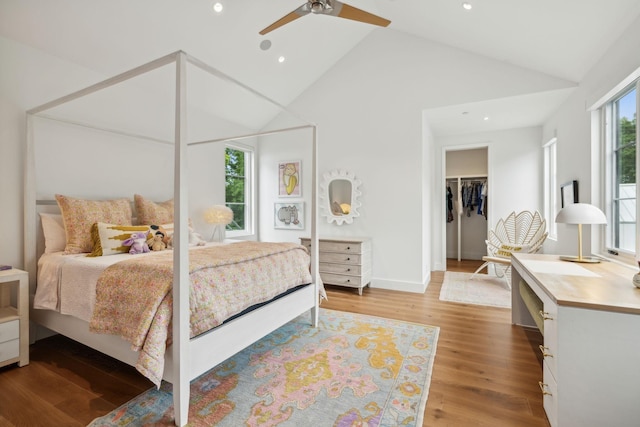 bedroom with high vaulted ceiling, a walk in closet, ceiling fan, light hardwood / wood-style floors, and a closet