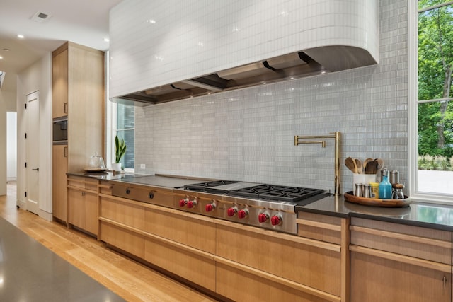 kitchen with premium range hood, light brown cabinetry, stainless steel gas stovetop, tasteful backsplash, and light hardwood / wood-style floors