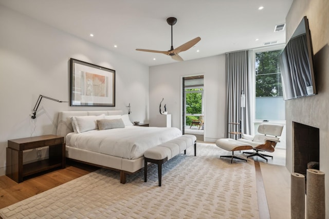 bedroom with ceiling fan, a fireplace, and light wood-type flooring