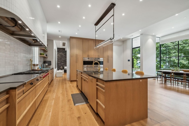 kitchen featuring light hardwood / wood-style flooring, hanging light fixtures, decorative backsplash, exhaust hood, and a large island with sink