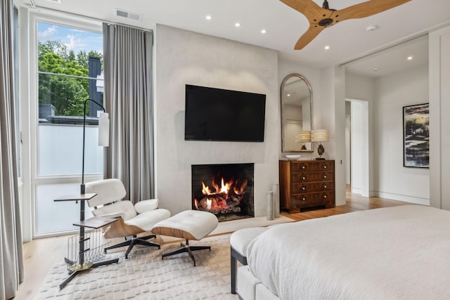 bedroom featuring a fireplace, ceiling fan, and light hardwood / wood-style floors