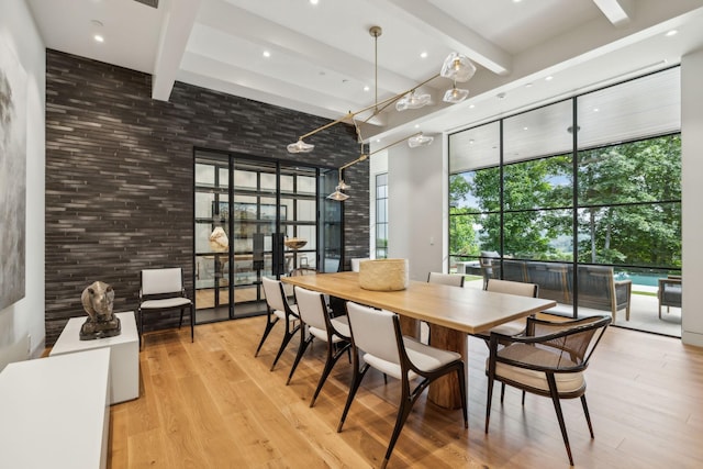 dining area with beamed ceiling, a wall of windows, and light hardwood / wood-style flooring