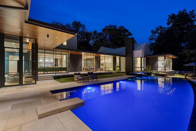 pool at night with a shed, a diving board, and a patio area