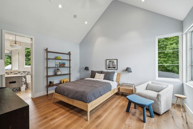 bedroom with multiple windows, high vaulted ceiling, ensuite bath, and light hardwood / wood-style floors