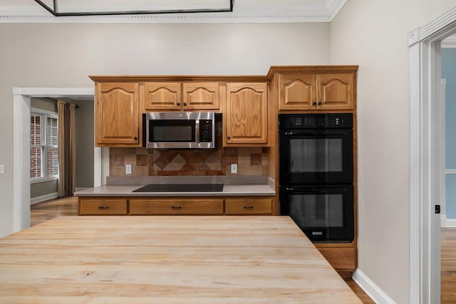 kitchen with brown cabinets, black appliances, butcher block counters, and tasteful backsplash