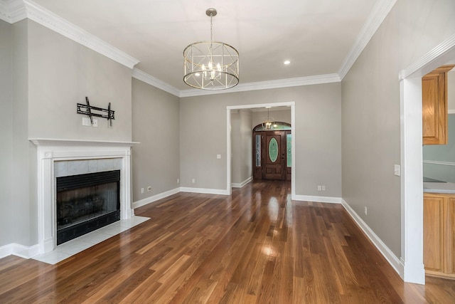 unfurnished living room featuring baseboards, dark wood finished floors, a tiled fireplace, crown molding, and a notable chandelier