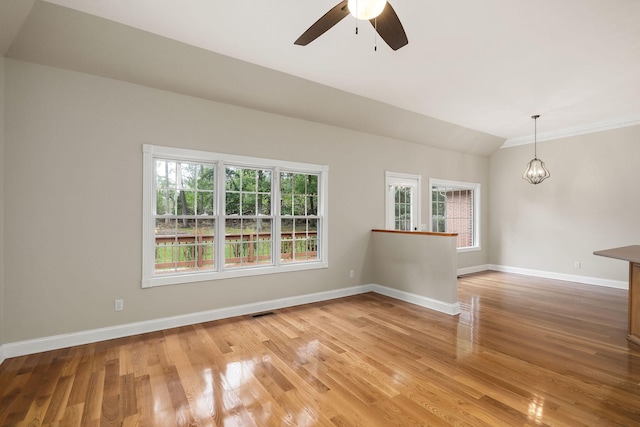 empty room featuring lofted ceiling, visible vents, wood finished floors, baseboards, and ceiling fan with notable chandelier