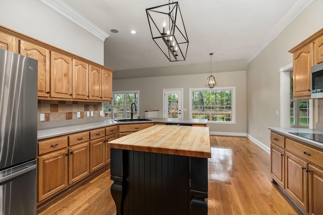 kitchen with butcher block countertops, a sink, a kitchen island, appliances with stainless steel finishes, and pendant lighting