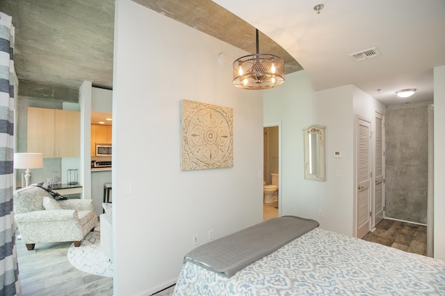 bedroom with hardwood / wood-style flooring, ensuite bathroom, a chandelier, and a closet