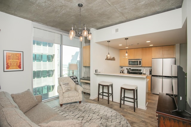 kitchen with hanging light fixtures, a kitchen breakfast bar, light brown cabinetry, appliances with stainless steel finishes, and hardwood / wood-style flooring