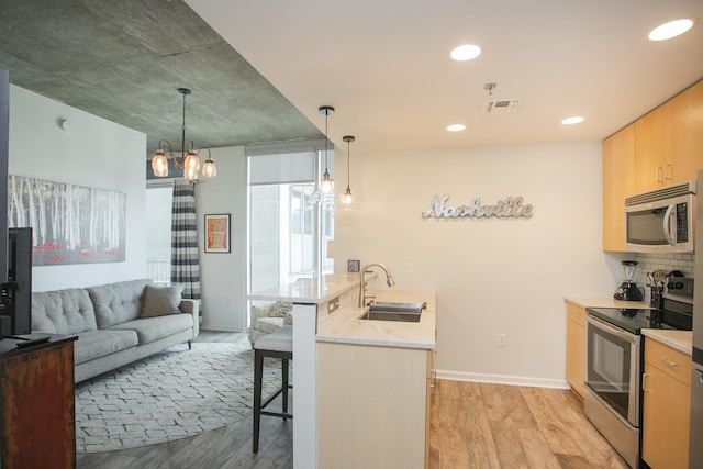 kitchen featuring sink, hanging light fixtures, stainless steel appliances, a breakfast bar area, and light wood-type flooring