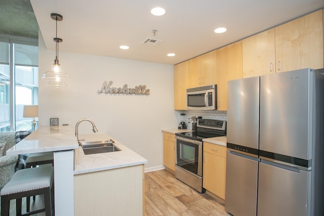 kitchen featuring hanging light fixtures, kitchen peninsula, light brown cabinetry, and appliances with stainless steel finishes