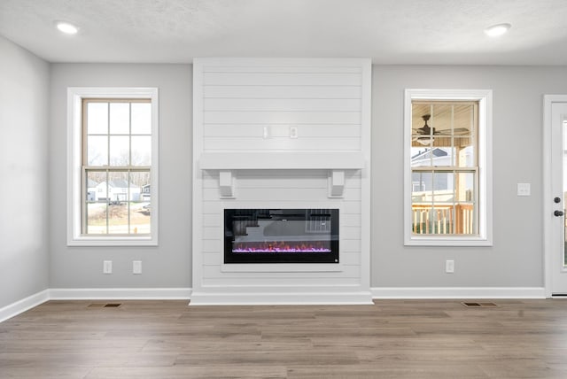 unfurnished living room featuring ceiling fan, a fireplace, a textured ceiling, and light hardwood / wood-style flooring