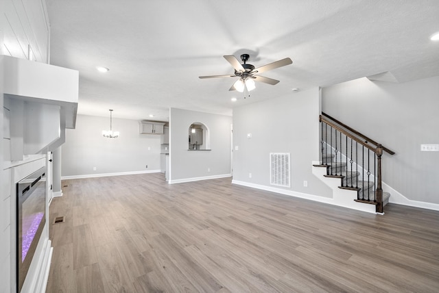 unfurnished living room featuring ceiling fan with notable chandelier and light hardwood / wood-style flooring