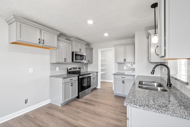 kitchen featuring sink, a textured ceiling, tasteful backsplash, light hardwood / wood-style floors, and stainless steel appliances