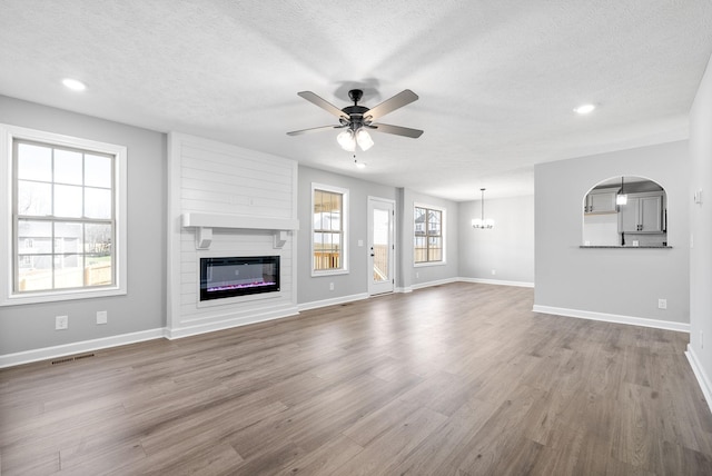 unfurnished living room with hardwood / wood-style floors, ceiling fan with notable chandelier, and a textured ceiling