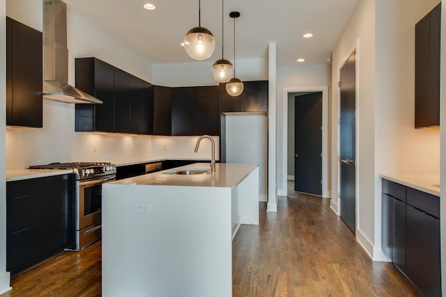 kitchen with a kitchen island with sink, sink, stainless steel gas range, wall chimney exhaust hood, and decorative light fixtures