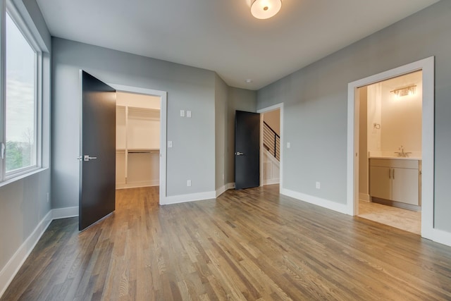 unfurnished bedroom featuring hardwood / wood-style floors, ensuite bathroom, a spacious closet, and a closet