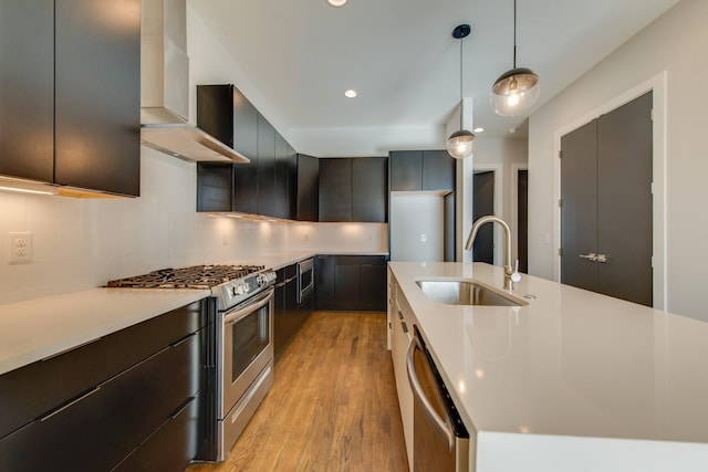 kitchen featuring sink, wall chimney exhaust hood, stainless steel appliances, backsplash, and pendant lighting