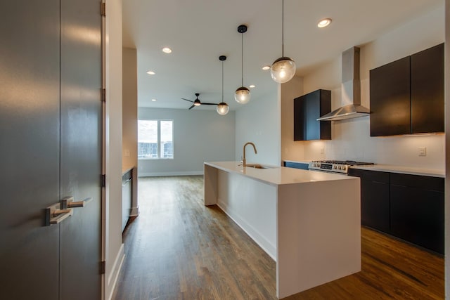 kitchen with pendant lighting, backsplash, a kitchen island with sink, wall chimney range hood, and sink