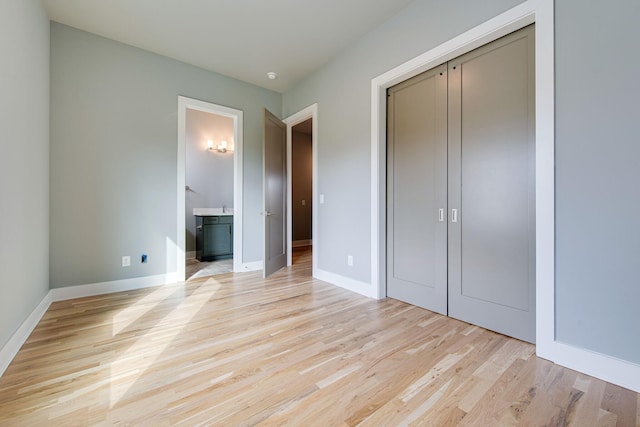 unfurnished bedroom featuring a closet, ensuite bath, and light hardwood / wood-style flooring