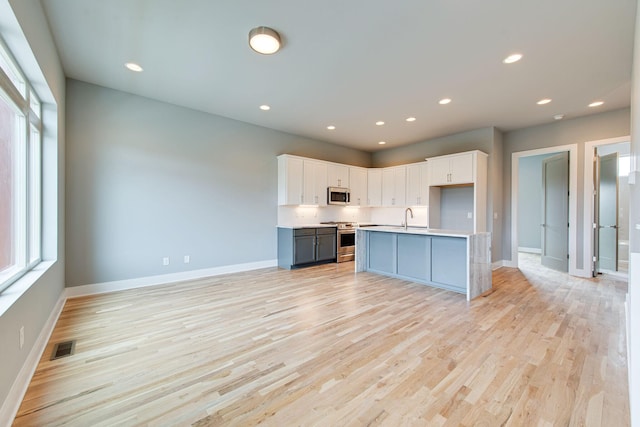 kitchen featuring sink, appliances with stainless steel finishes, light hardwood / wood-style floors, an island with sink, and white cabinets