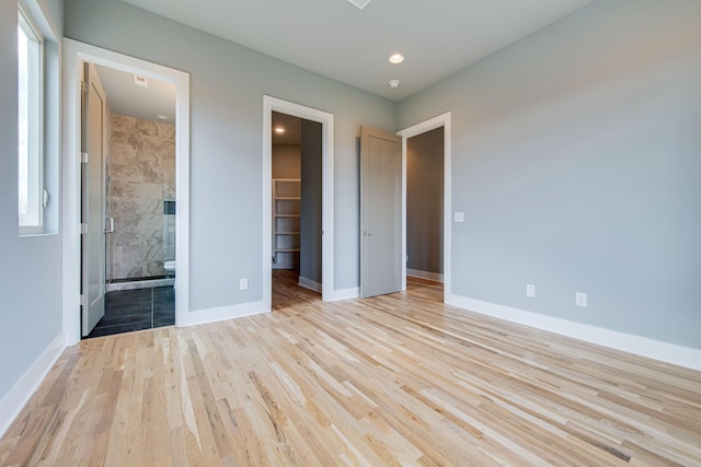 unfurnished bedroom featuring multiple windows, a closet, a walk in closet, ensuite bath, and light hardwood / wood-style flooring