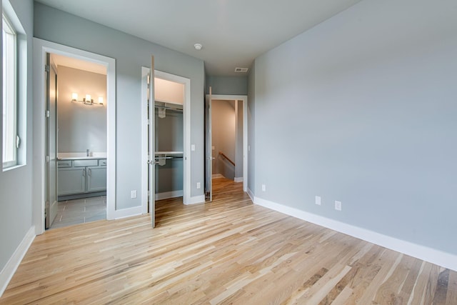 unfurnished bedroom with a walk in closet, light hardwood / wood-style floors, and ensuite bathroom