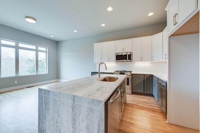 kitchen featuring sink, white cabinetry, stainless steel appliances, light stone countertops, and an island with sink