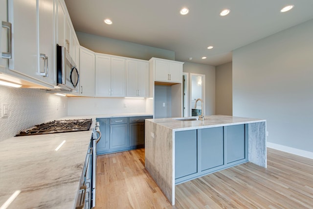 kitchen with an island with sink, appliances with stainless steel finishes, white cabinets, and light stone counters