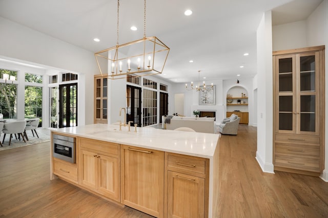 kitchen featuring a large island, sink, light brown cabinets, decorative light fixtures, and light wood-type flooring