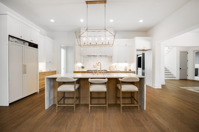 kitchen with a kitchen island with sink, sink, paneled built in fridge, white cabinets, and hanging light fixtures