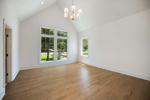 spare room featuring wood-type flooring, high vaulted ceiling, and an inviting chandelier