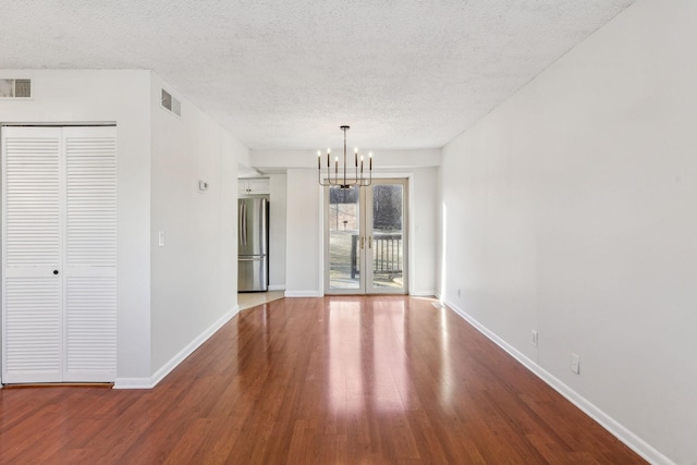 unfurnished room featuring a chandelier, wood-type flooring, french doors, and a textured ceiling