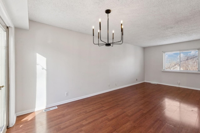 unfurnished dining area with dark wood-type flooring, a textured ceiling, and an inviting chandelier