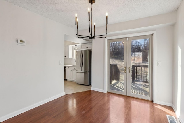 unfurnished dining area with a chandelier, a textured ceiling, light hardwood / wood-style floors, and french doors