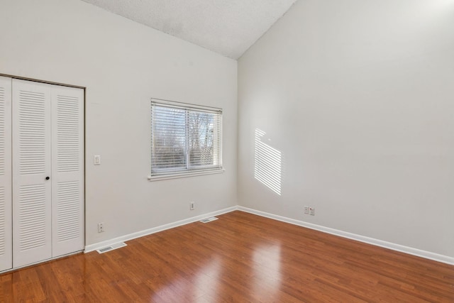 unfurnished bedroom featuring hardwood / wood-style flooring, vaulted ceiling, a textured ceiling, and a closet