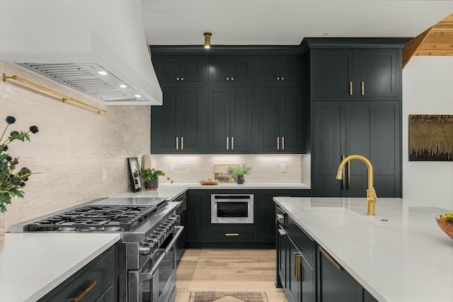 kitchen with light wood-type flooring, custom range hood, backsplash, and stainless steel appliances